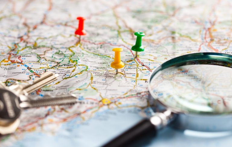 Map With Thumbtacks and Magnifying Glass